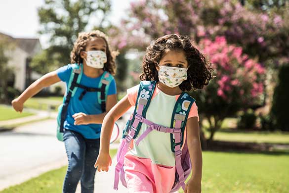 two-girls-running-to-school-wearing-backpacks-and-masks